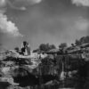 A black and white photo of two people standing on top of a cliff.
