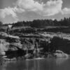 A man standing on the side of a river near some rocks.