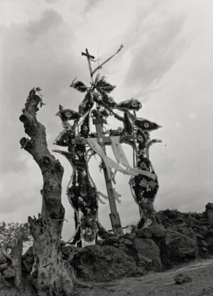 A black and white photo of a cross on top of a tree.