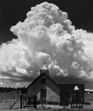 A black and white photo of a church with clouds in the background.