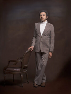 A man in a suit standing next to a chair.