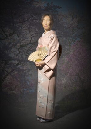 A woman in pink kimono holding an open fan.