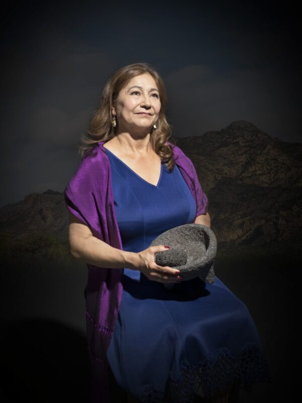 A woman in blue dress holding a hat.