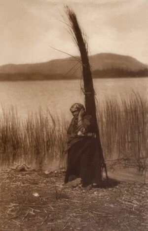 A woman sitting in front of a tree near the water.