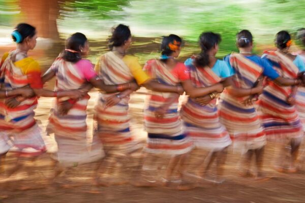 A group of women in colorful dresses walking on dirt.