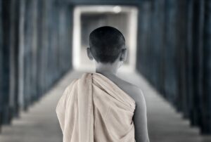 A young monk in a white robe is standing in the hallway.