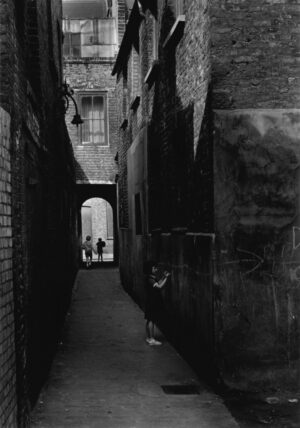 A black and white photo of an alley with two people walking.
