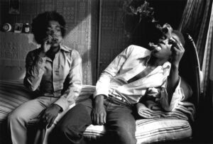 Two men sitting on a couch smoking and talking.