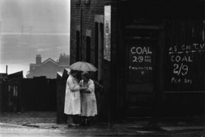 Two women standing under an umbrella on a rainy day.
