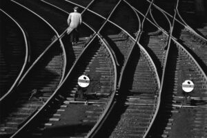 A man walking on train tracks near many other trains.