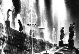 A black and white photo of fountains in the middle of a city.