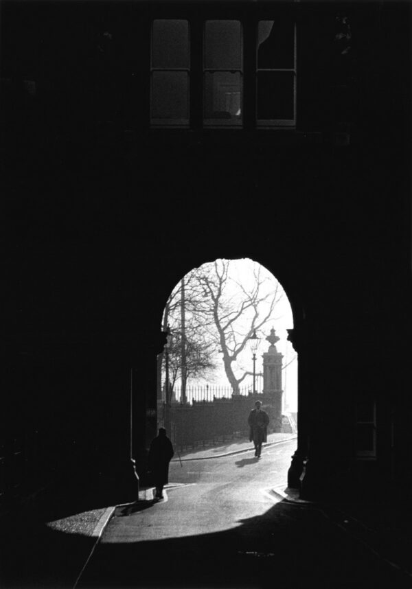 A person walking through an arch on the sidewalk.