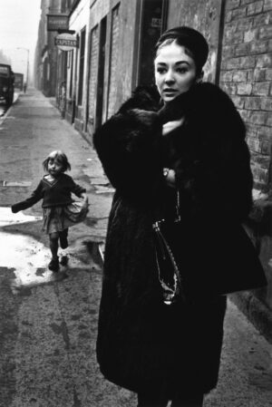 A woman in black coat holding purse while standing on sidewalk.