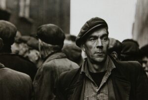 A man in a hat and jacket standing next to other men.