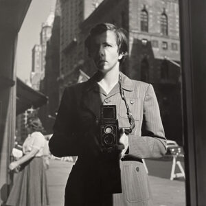 A man holding an old camera in front of a building.