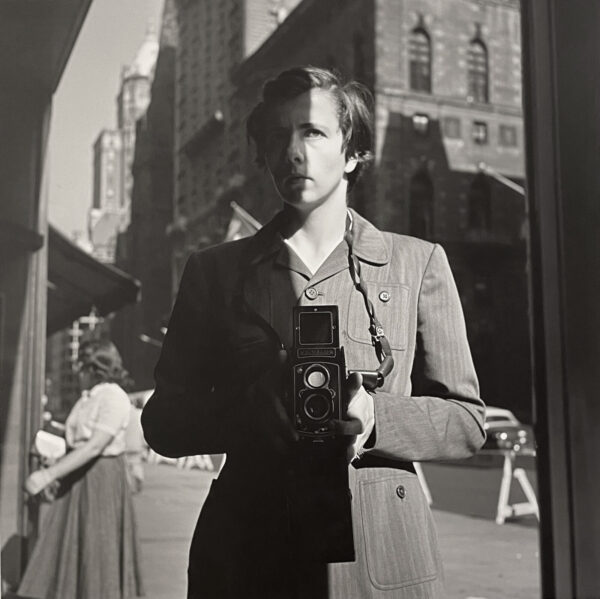 A man holding an old camera in front of a building.