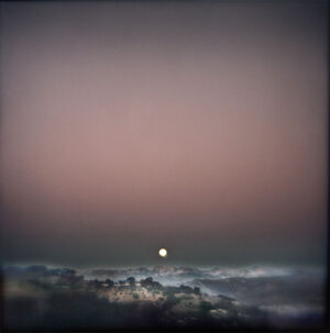 A full moon setting over the ocean at dusk.