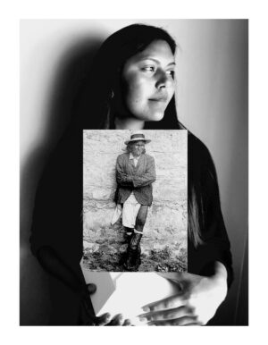A woman holding up an old photograph of herself.