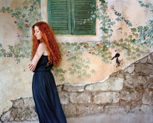 A woman in black dress leaning against wall.