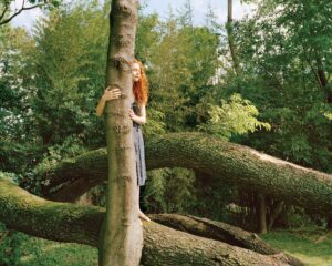 A woman leaning on a tree in the woods.