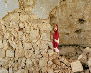 A child in red is standing on the rubble of an old building.