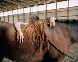 A woman is hugging the back of a horse.