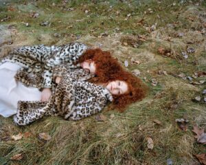 A woman laying in the grass wearing a leopard print coat.