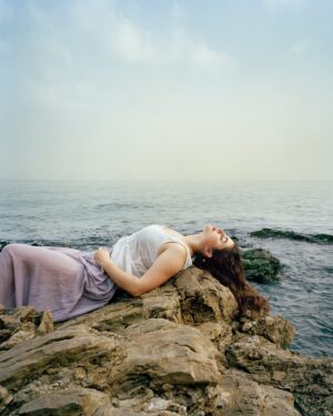 A woman laying on the rocks near water.