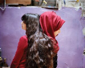 Two women with long hair and a red head covering.