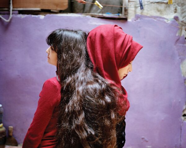 Two women with long hair and a red head covering.