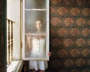 A woman in white dress holding onto an old window.