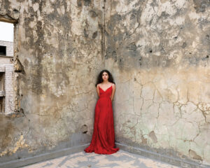 A woman in red dress standing next to a wall.