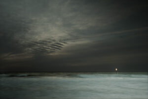 A dark sky with clouds and water in the foreground.