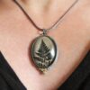 A person wearing a necklace with a picture of a fern.