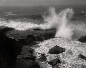A black and white photo of waves crashing on rocks.