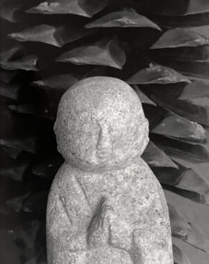 A stone statue of a person in front of some trees.