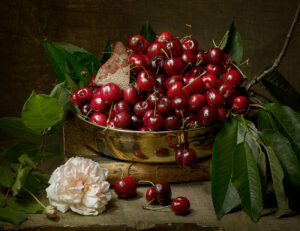 A bowl of cherries on the table with flowers.