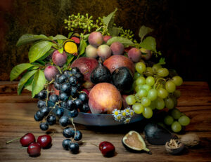 A bowl of fruit on a table with other fruits.