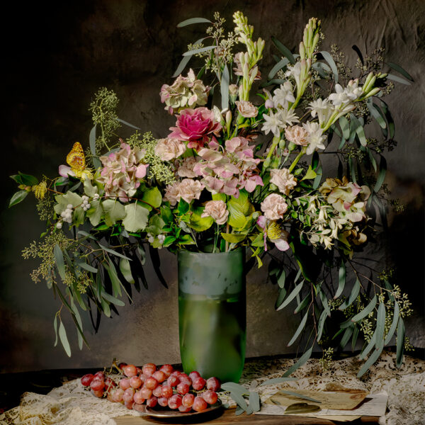 A vase of flowers and grapes on the table.