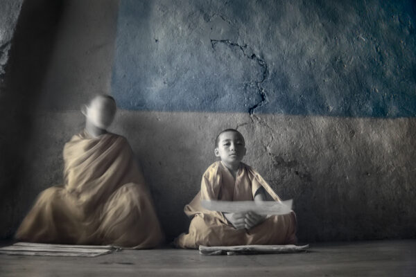 Two young monks sitting in a room with a wall behind them.