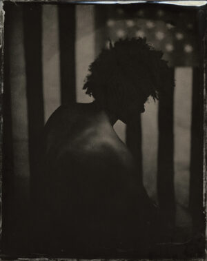 A man with dreadlocks is standing in front of an american flag.