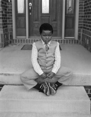 A young man sitting on the steps of his home.