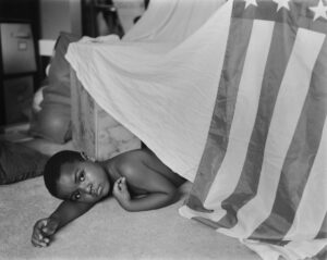 A young boy laying on the ground under an american flag.