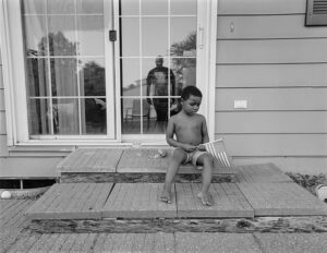 A young boy sitting on the steps of his house.