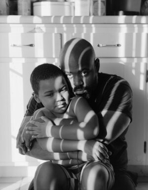 A man and boy sitting on the floor hugging.