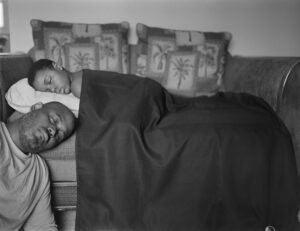 A man and child sleeping in bed under the covers.