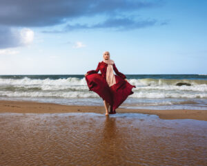 A woman in red dress standing on the beach.