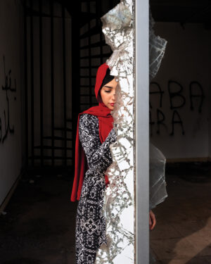 A woman in black and white dress leaning against wall.