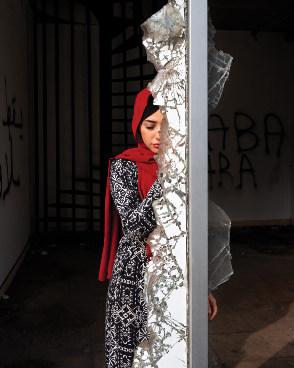 A woman in black and white dress leaning against wall.