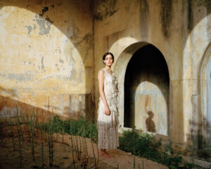 A woman in white dress standing next to an arch.